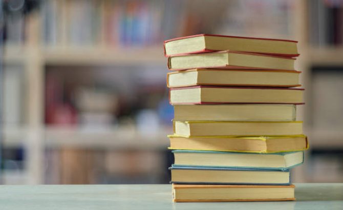 Stack of books with blurred bookshelf background, reading, learning, education or home office concept
